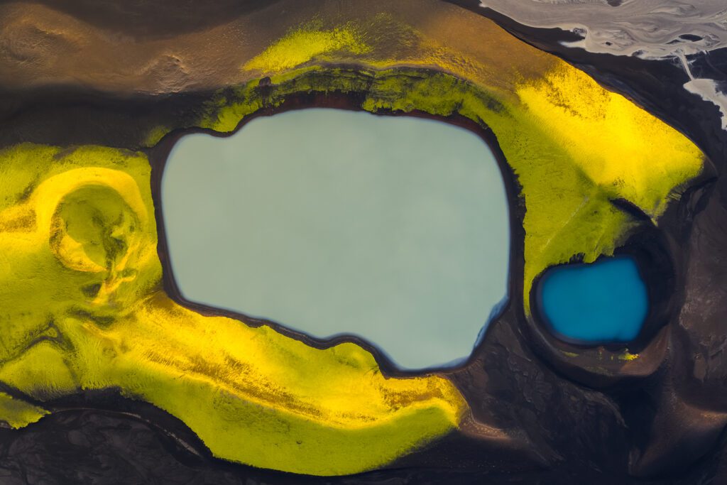 Top-down aerial of a turquoise lake with vivid yellow moss banks and a small blue pool beside it.