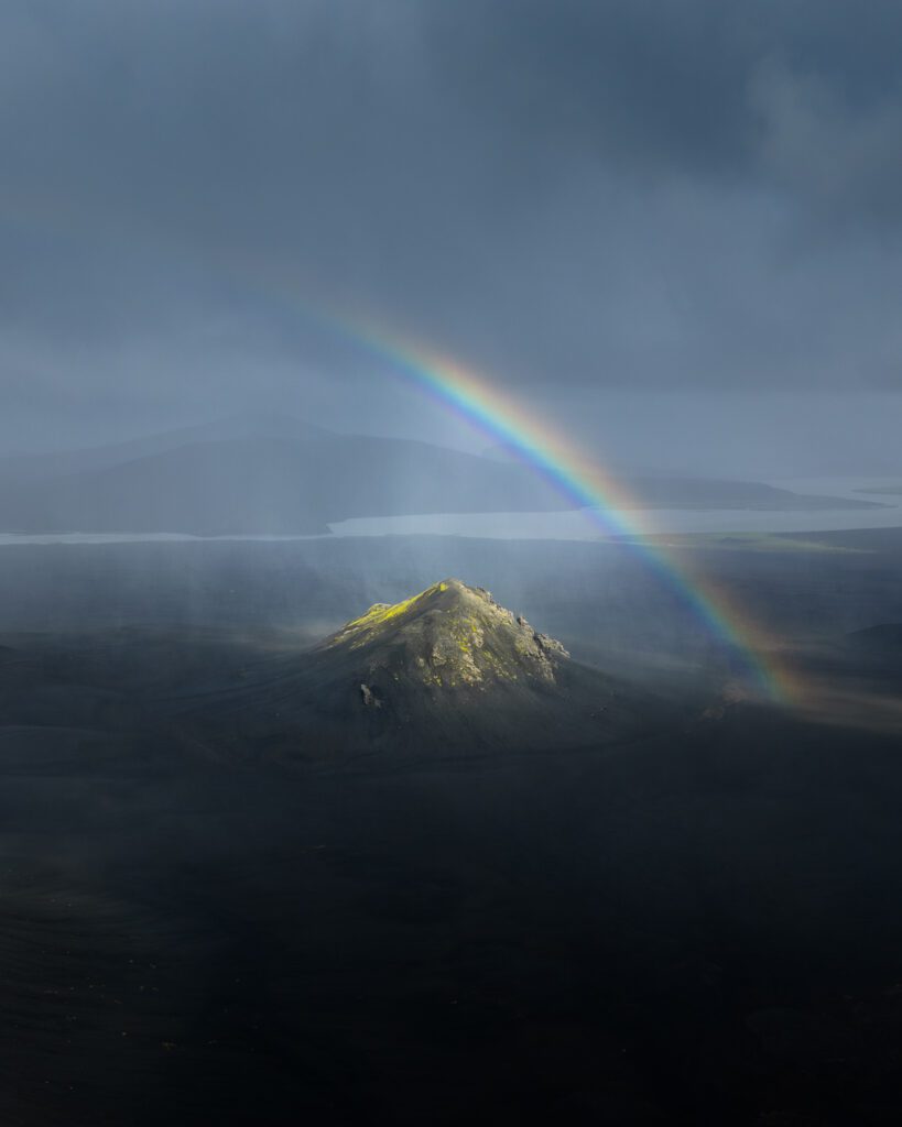 Aerial drone view of moss-covered slopes meeting a black sand plain in the Icelandic Highlands.