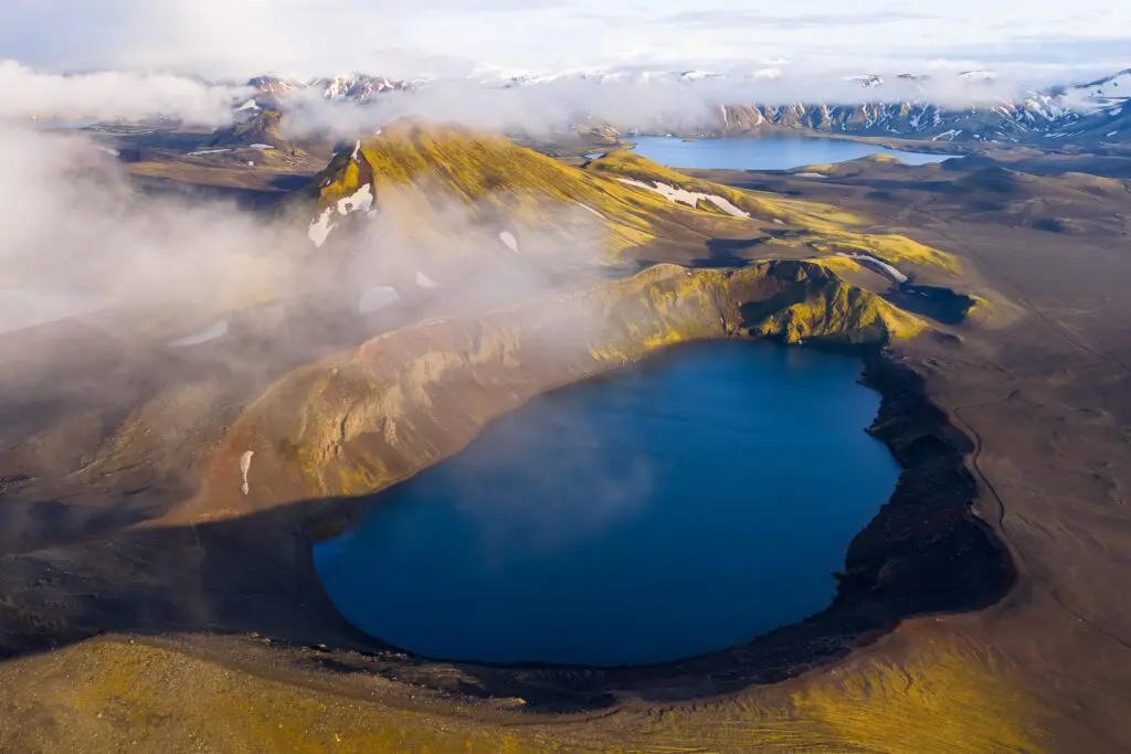 Aerial drone view of Bláhylur crater lake, ringed by golden moss and rust-red scoria slopes in Fjallabak, Iceland.