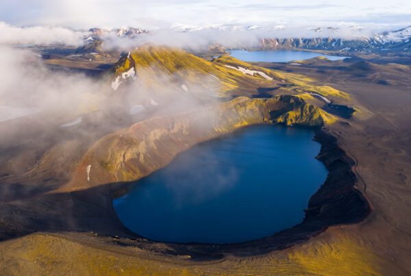 Aerial drone view of Bláhylur crater lake, ringed by golden moss and rust-red scoria slopes in Fjallabak, Iceland.