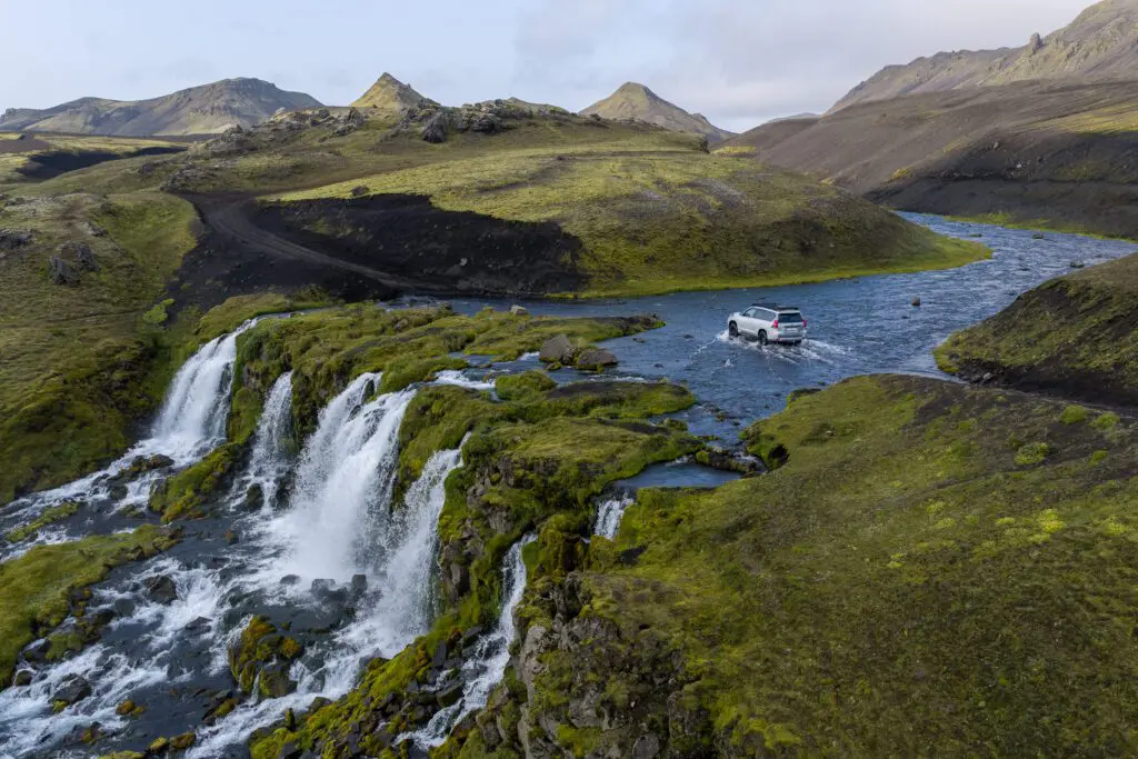 A modified 4x4 crossing a highland river beside a run of waterfalls in the Icelandic Highlands